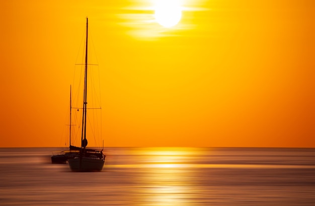 Sailing boat in sunset or sunrise sky over sea with a stunning tropical sunset and smooth waves effect Motion blur background Colorful golden sky seascape