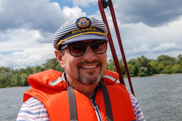 Sailor man in a cap on a boat under sail against the sky and water