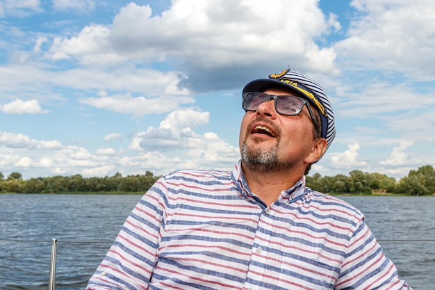 Sailor man in a cap on a boat under sail against the sky and water