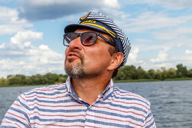 Sailor man in a cap on a boat under sail against the sky and water