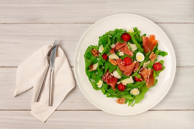 salad, arugula leaves  with parma prosciutto cherry quail eggs in a plate on wooden background