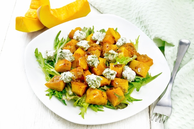 Salad of baked pumpkin, arugula with balls of salt cheese, seasoned with honey, mustard, garlic and vegetable oil in a plate, towel and fork