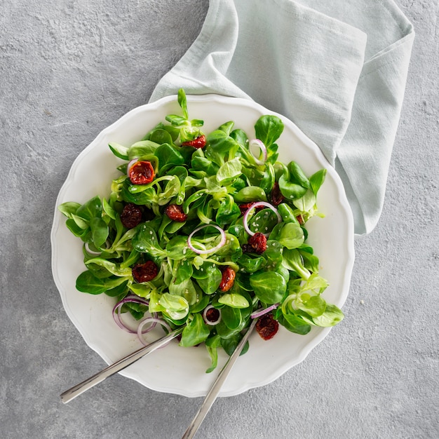 Salad bowl mache leaves baked tomatoes concrete background top view