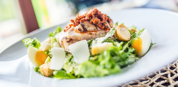 Salad caesar with grilled pieces of chicken breasts on white plate in restaurant.