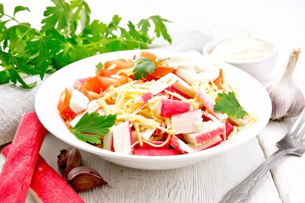 Salad of crab sticks cheese garlic tomatoes and mayonnaise kitchen towel parsley on the background of a light wooden board