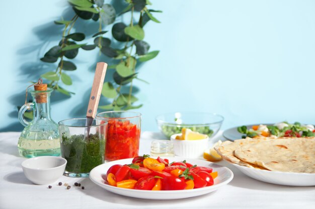 Salad of fresh cherry tomatoes with basil on the dinner table with dips, radish salad, pita flat bread