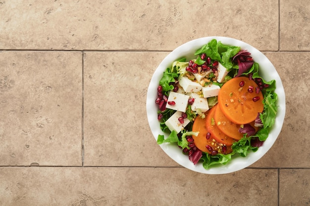 Salad Fresh green salad with feta cheese persimmon pomegranate and pistachio on white plate Idea for healthy delicious winter Christmas salad Healthy balanced eating Top view