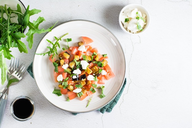 Salad of fried eggplant tomato and feta cheese on a plate on the table Homemade lunch Top view