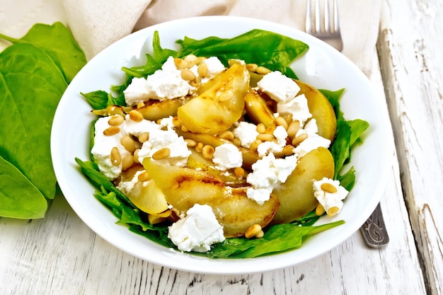 Salad of fried pear spinach salted feta cheese and cedar nuts in a plate napkin on a light wooden board background