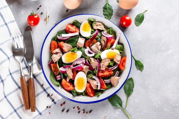 Salad from the liver of codfish, eggs, spinach and tomato on a white plate on a light slate, stone or concrete background