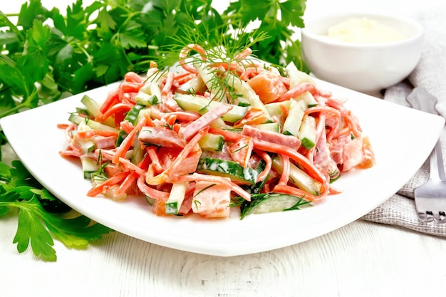 Salad from smoked sausage, spicy carrot, tomato, cucumber and spices, dressed with mayonnaise, towel, fork and parsley on a wooden board background