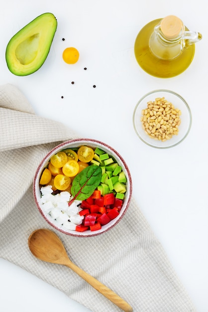 Salad of goat cheese, avocado, pepper, tomato and herbs in a bowl.