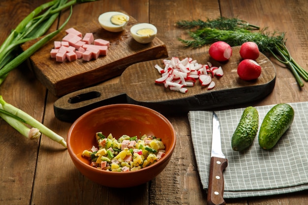 Salad ingredients in a bowl and over cutting boards on wooden background