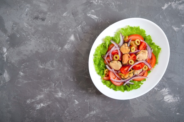 Salad of marinated mussels, fresh tomatoes, red onions, olives in a white bowl. The top view