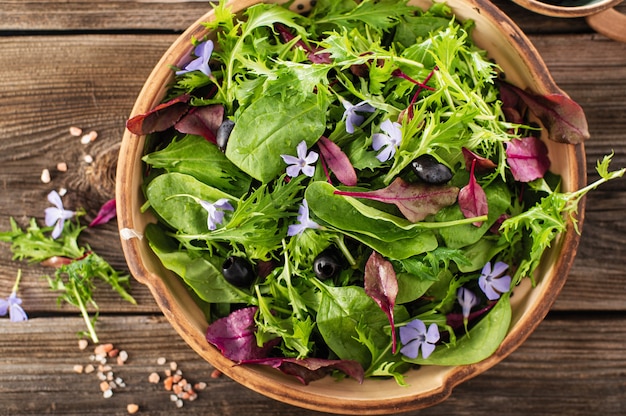 Salad mix with baby spinach mizuna salad edible flowers and olives on a wooden background