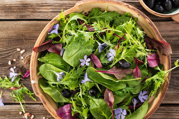 Salad mix with baby spinach mizuna salad edible flowers and olives on a wooden background