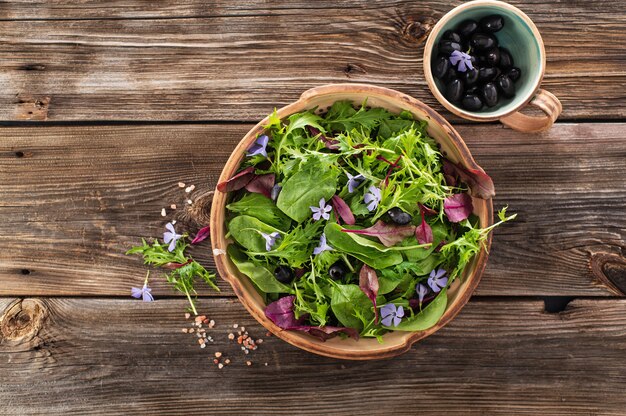 Salad mix with baby spinach mizuna salad edible flowers and olives on a wooden background