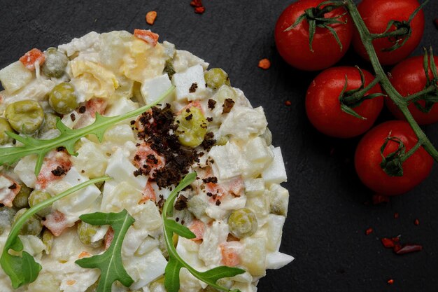 Salad Olivier on black slate on a black background with tomatoes Close up