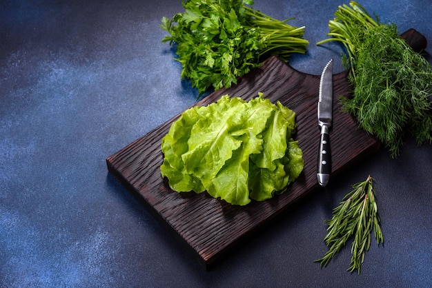 Salad parsley and dill on a dark cutting board against a blue concrete background