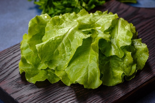 Salad parsley and dill on a dark cutting board against a blue concrete background