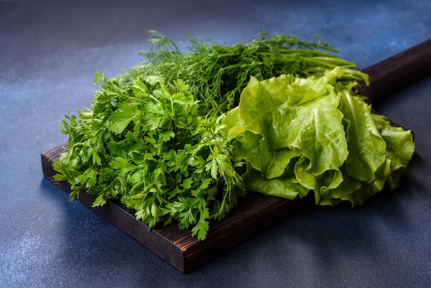 Salad parsley and dill on a dark cutting board against a blue concrete background