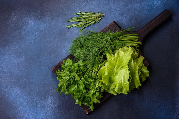 Salad parsley and dill on a dark cutting board against a blue concrete background