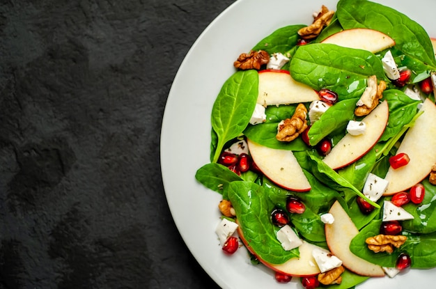 Salad of spinach, apples, pomegranate, cheese, walnuts on a stone background