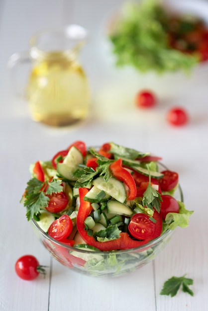 Salad on a white wooden background from tomatoes, cucumber, lettuce and red pepper. Healthy eating concept.