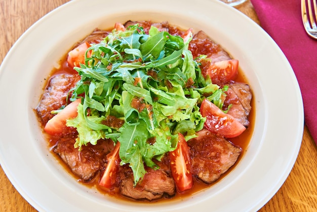 Salad with arugula leaves fried meat and tomato on table