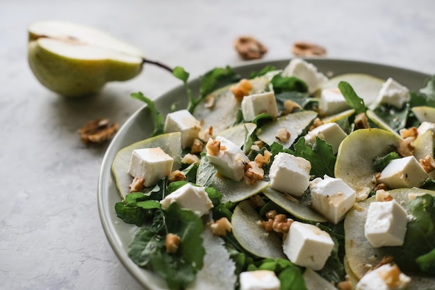 Salad with arugula pear feta cheese and walnuts Delicacy salad on a plate on a gray background