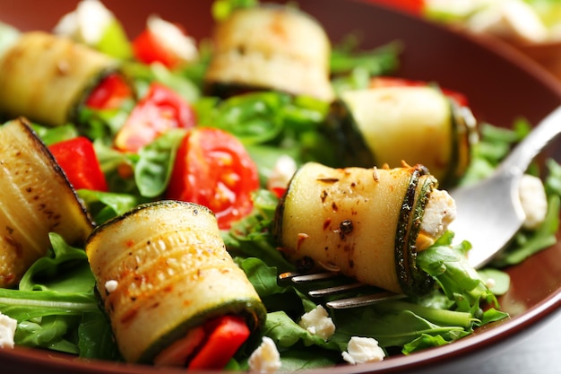 Salad with arugula and zucchini rolls on plate on table background