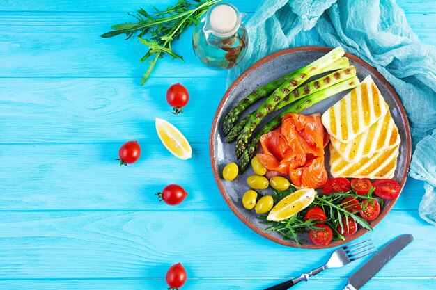 Photo salad with asparagus, grilled halloumi cheese, salmon fillet, tomatoes, arugula and green olives. top view