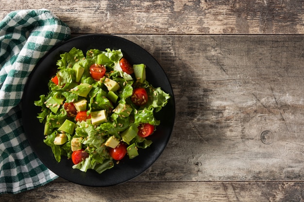 Photo salad with avocado, lettuce, tomato and flax seeds on wooden table top view copy space