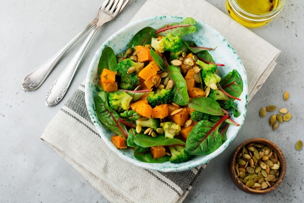 Salad with a baked pumpkin, chard, broccoli, and pumpkin seeds in ceramic plate on stone or concrete table.  Rustic style.  