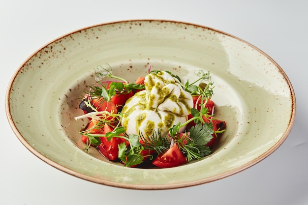 Salad with buratta cheese tomatoes parsley and dill and pesto sauce in plate on white background