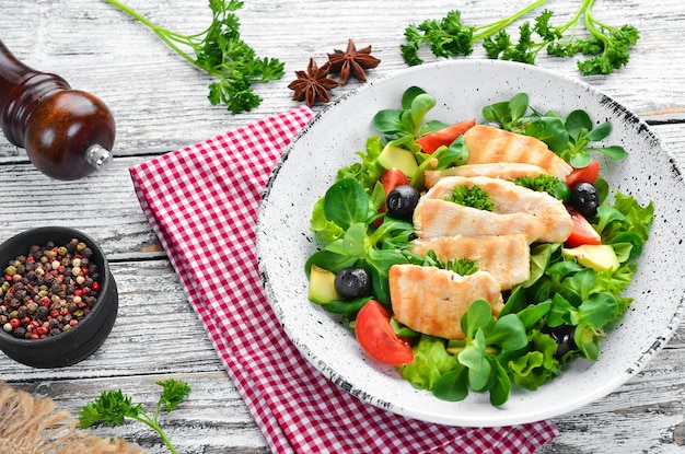 Salad with chicken fillet olives tomatoes and avocados in a plate on a wooden background Top view Free space for your text Flat lay