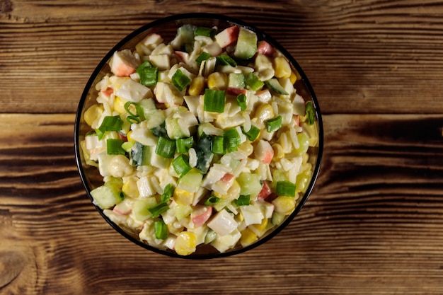 Salad with crab sticks, sweet corn, cucumber, eggs, rice and mayonnaise on wooden table. Top view