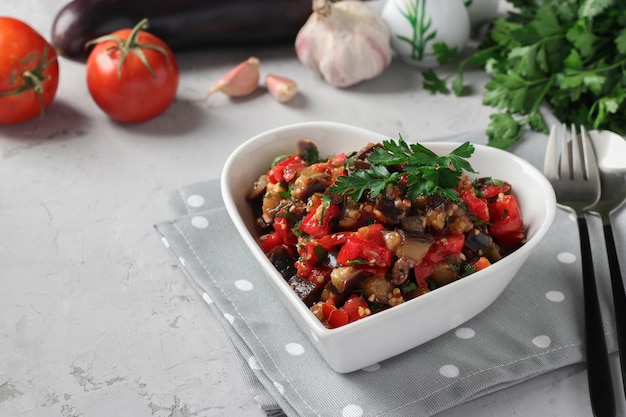 Salad with eggplants tomatoes garlic and parsley in a plate in the shape of a heart on a light gray background