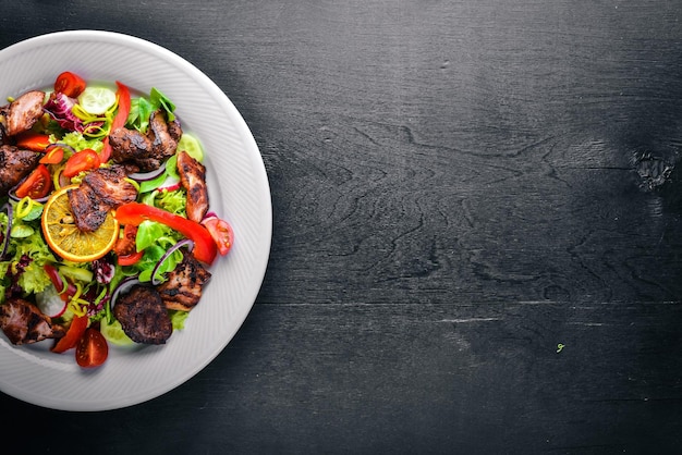 Salad with fresh cucumbers tomatoes and greens with grilled meat on a plate Wooden board Top view Free space