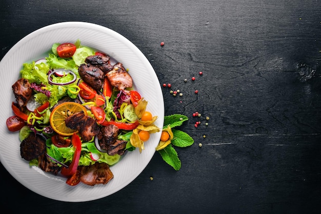 Salad with fresh cucumbers tomatoes and greens with grilled meat on a plate Wooden board Top view Free space