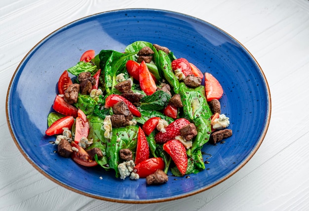 Salad with fried duck liver brie cheese strawberries tomatoes and spinach leaves