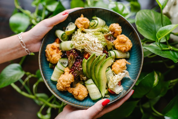 Salad with fried fish avocado tomatoes cucumbers and herbs in woman hands