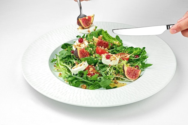 Salad with goat cheese and figs in a white plate on a white tablecloth Closeup selective focus