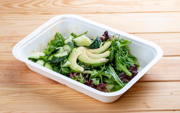 Salad with greens and avocado Vegetarian food Takeaway food On a wooden background