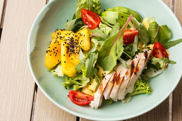 Salad with grilled chicken, mango, lettuce, avocado, tomatoes, arugula, cheese sause on a white plate