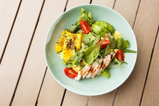 Salad with grilled chicken, mango, lettuce, avocado, tomatoes, arugula, cheese sause on a white plate