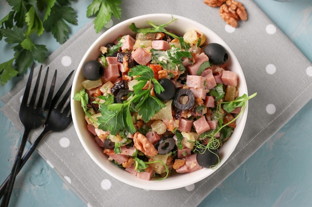 Salad with ham pineapple black olives and walnuts in a white bowl on a blue background