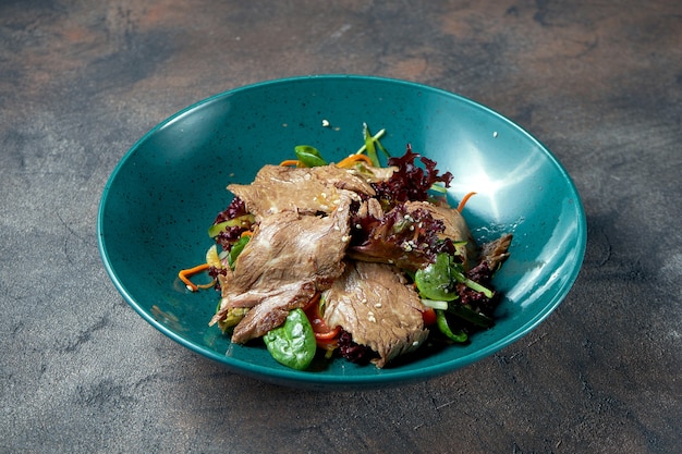 Salad with juicy roast beef, herbs and tomatoes in a plate on a dark background