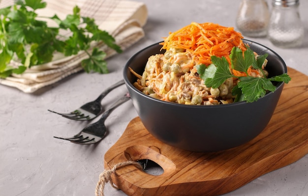 Salad with Korean carrots meat and canned peas in dark bowl on wooden board