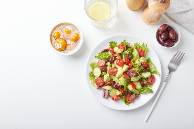 Salad with lettuce cucumbers tomatoes olives and avocados in white plate on the table